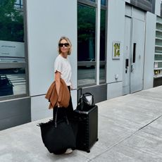 Stylist and fashion editor Natalie Cantell on her way to the airport wearing a neutral travel outfit with Celine sunglasses, Vuori sweatpants, a Nordstrom cashmere sweater, H&M t-shirt, Adidas Sambas, Toteme T-Lock bag, Naghedi oversize tote, and an Away suitcase.