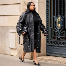 A street style image of a woman wearing an all-black outfit that consists of a long leather coat, a dress, pointed toe heels, and a Bottega Veneta Cassette Bag.