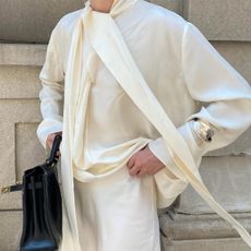 Christie Tyler wearing a cream silk scarf blouse with a lace-trim matching skirt.